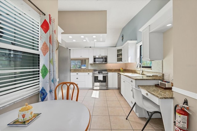 kitchen with tasteful backsplash, white cabinetry, light tile patterned floors, stainless steel appliances, and light stone countertops