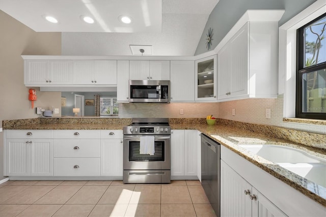 kitchen with white cabinetry, light tile patterned floors, stainless steel appliances, light stone countertops, and decorative backsplash