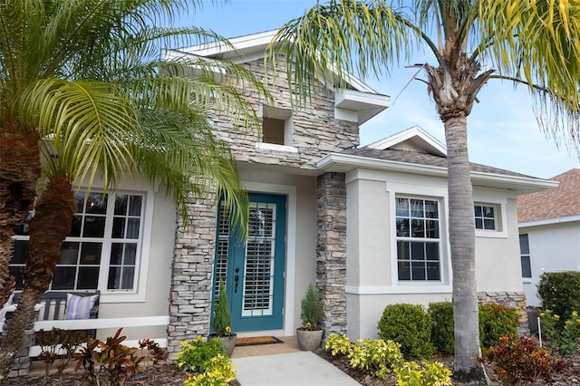 doorway to property with stone siding, a shingled roof, and stucco siding