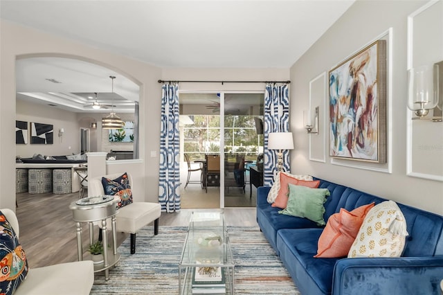 living area with visible vents, a tray ceiling, arched walkways, and wood finished floors