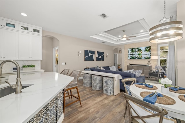 dining room featuring visible vents, arched walkways, wood finished floors, a tray ceiling, and recessed lighting