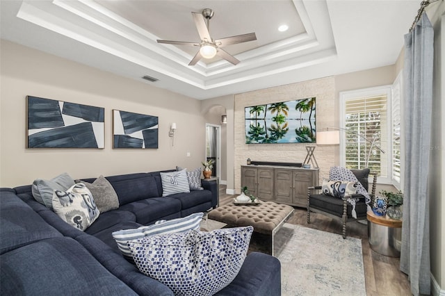 living area featuring arched walkways, wood finished floors, a raised ceiling, and visible vents