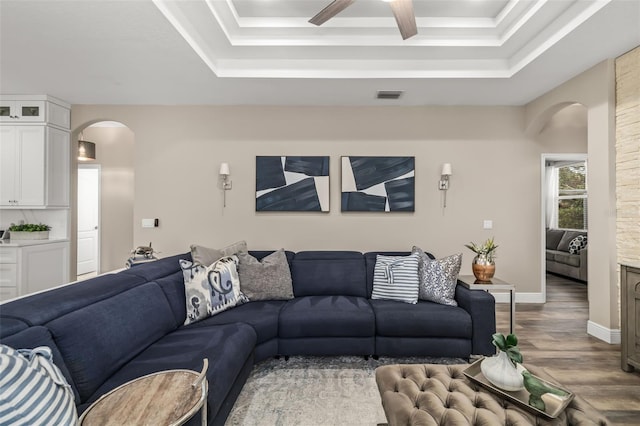 living room featuring visible vents, arched walkways, a tray ceiling, and wood finished floors