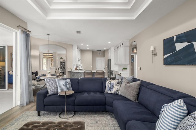 living room featuring light wood-type flooring, a raised ceiling, visible vents, and recessed lighting