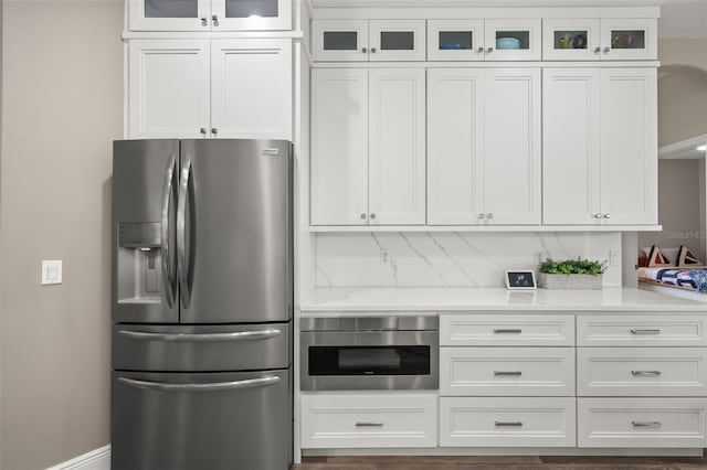 kitchen featuring light stone counters, stainless steel refrigerator with ice dispenser, decorative backsplash, glass insert cabinets, and white cabinetry