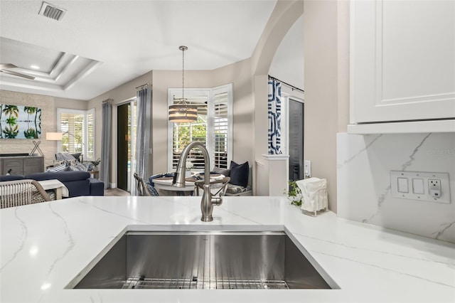 interior space featuring arched walkways, light stone counters, a sink, visible vents, and white cabinets