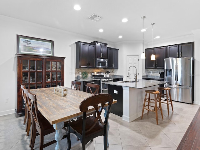 kitchen with crown molding, appliances with stainless steel finishes, a kitchen island with sink, a sink, and a kitchen breakfast bar