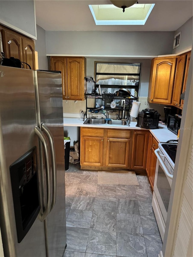 kitchen featuring a skylight, stainless steel refrigerator with ice dispenser, sink, and white range with electric cooktop