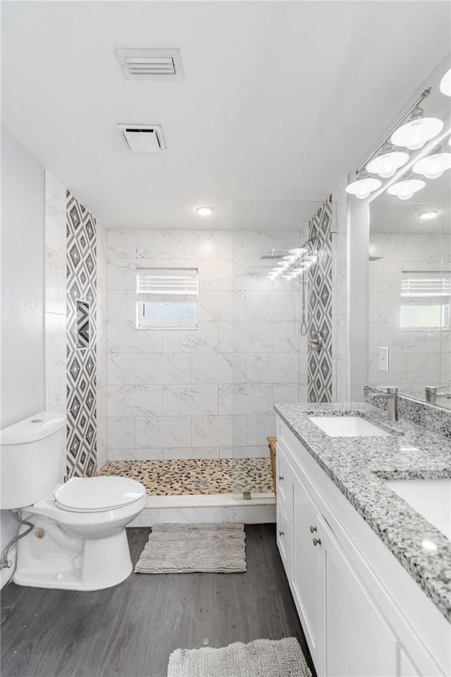 bathroom with hardwood / wood-style flooring, vanity, a tile shower, and toilet