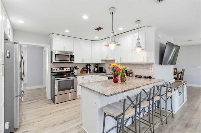 kitchen with a breakfast bar, appliances with stainless steel finishes, white cabinets, decorative light fixtures, and kitchen peninsula