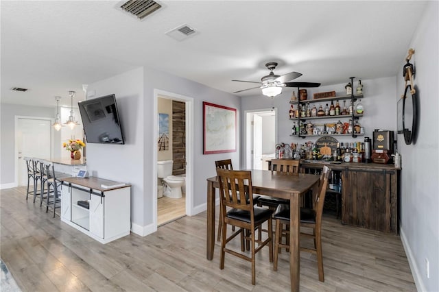 dining room with bar area, ceiling fan with notable chandelier, and light hardwood / wood-style flooring