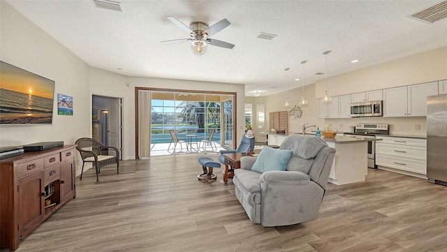 living room featuring ceiling fan, a textured ceiling, and light hardwood / wood-style flooring