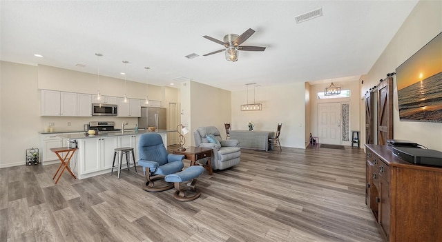 living room with a barn door, ceiling fan, and light wood-type flooring