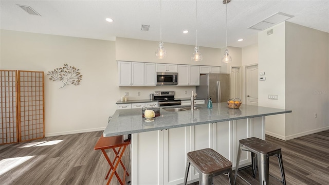 kitchen featuring a kitchen bar, sink, white cabinetry, decorative light fixtures, and appliances with stainless steel finishes