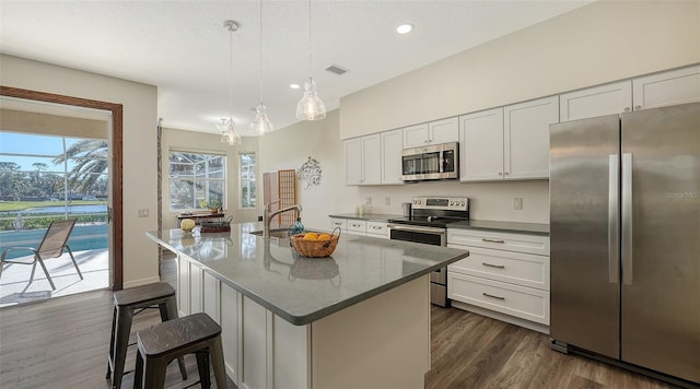 kitchen with appliances with stainless steel finishes, pendant lighting, white cabinets, a kitchen breakfast bar, and a kitchen island with sink