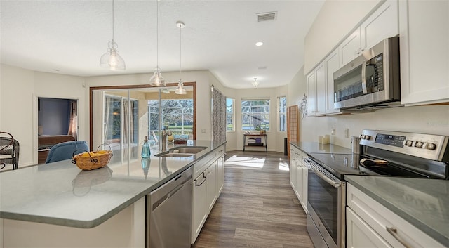 kitchen featuring white cabinetry, appliances with stainless steel finishes, pendant lighting, and a center island with sink