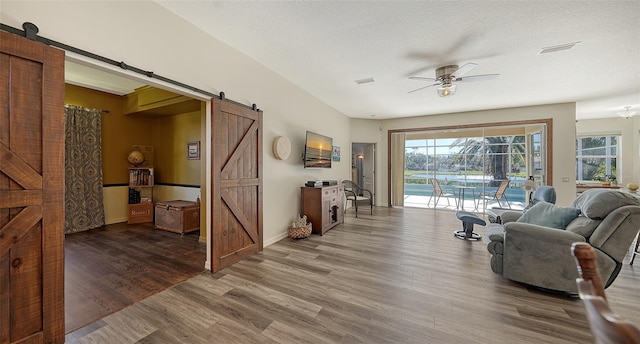 living room with a textured ceiling, wood-type flooring, a barn door, and ceiling fan