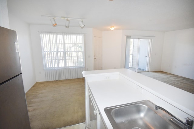 kitchen featuring white cabinetry, sink, stainless steel fridge, track lighting, and light carpet