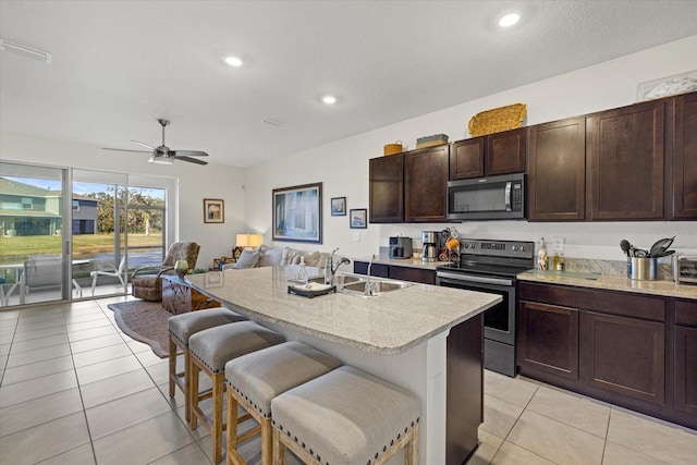 kitchen with sink, light tile patterned floors, appliances with stainless steel finishes, a kitchen breakfast bar, and a kitchen island with sink