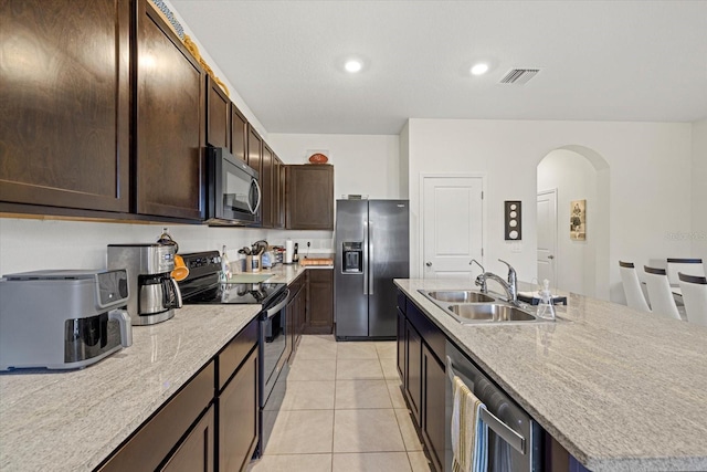 kitchen featuring appliances with stainless steel finishes, sink, light tile patterned floors, dark brown cabinetry, and a center island with sink