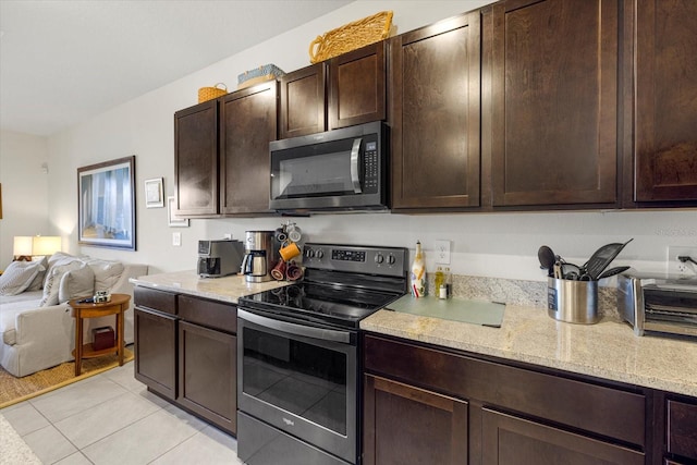 kitchen with dark brown cabinetry, appliances with stainless steel finishes, light stone countertops, and light tile patterned floors