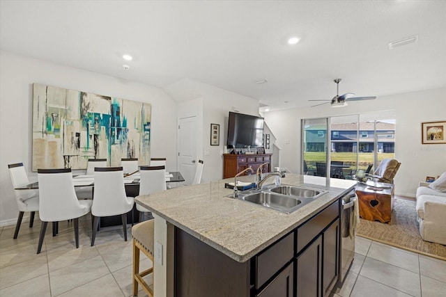 kitchen featuring light tile patterned flooring, sink, stainless steel dishwasher, dark brown cabinetry, and a center island with sink