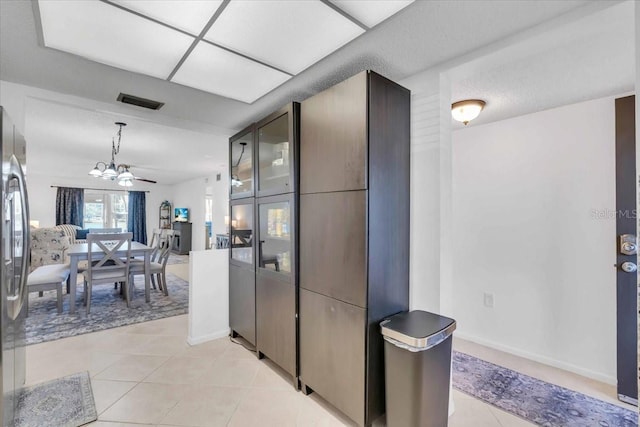 kitchen featuring a chandelier, stainless steel refrigerator, light tile patterned floors, and dark brown cabinetry