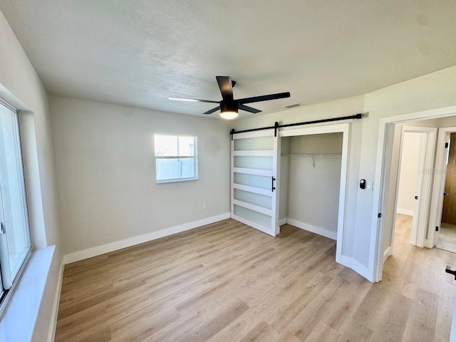 unfurnished bedroom with light hardwood / wood-style flooring, ceiling fan, a barn door, a textured ceiling, and a closet