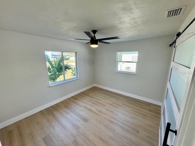 empty room with ceiling fan, a barn door, light hardwood / wood-style floors, and a textured ceiling