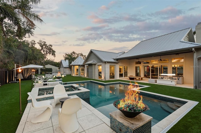 pool at dusk with ceiling fan, a patio, a yard, and a fire pit