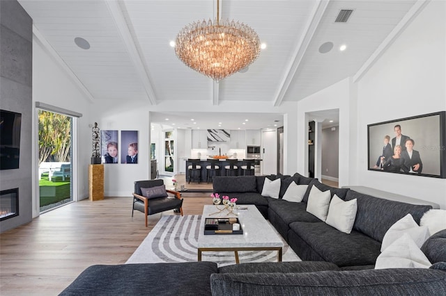 living room featuring beam ceiling, a fireplace, a chandelier, and light hardwood / wood-style flooring