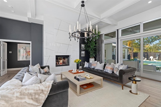 living room featuring beamed ceiling, an inviting chandelier, a tile fireplace, and light hardwood / wood-style flooring