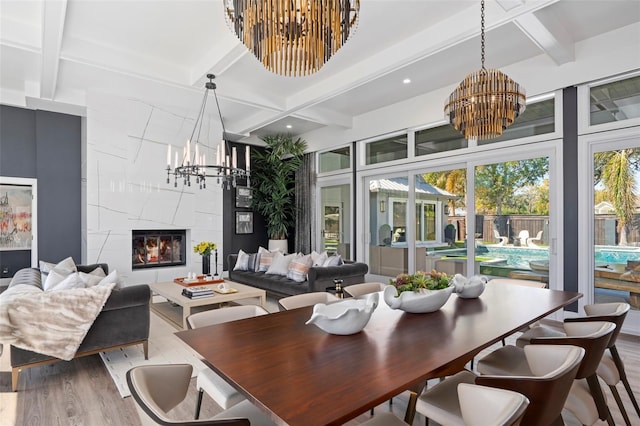 dining area featuring an inviting chandelier, wood-type flooring, a premium fireplace, and beamed ceiling