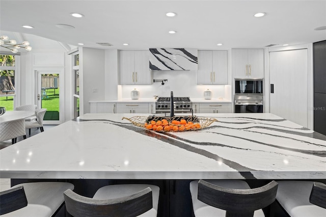 kitchen with a breakfast bar, stainless steel appliances, light stone counters, ventilation hood, and white cabinets