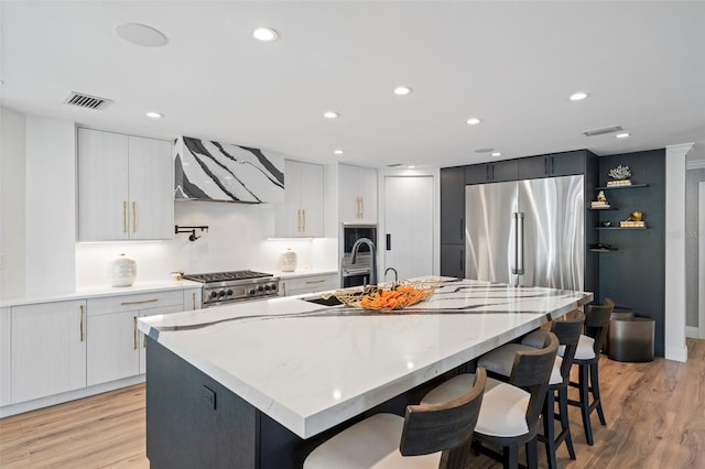 kitchen featuring a large island, stainless steel fridge, stove, range hood, and white cabinets