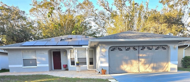 ranch-style house with an attached garage, driveway, roof with shingles, roof mounted solar panels, and stucco siding