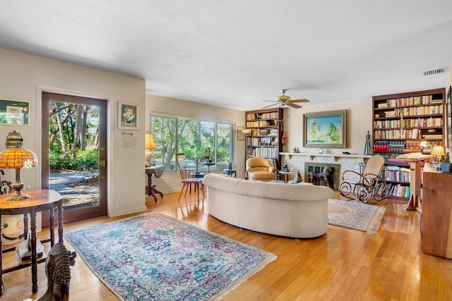 living room featuring a brick fireplace, hardwood / wood-style floors, and ceiling fan