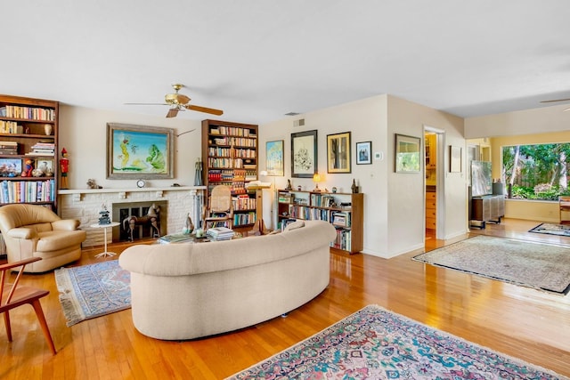 living room featuring a brick fireplace, light hardwood / wood-style flooring, and ceiling fan