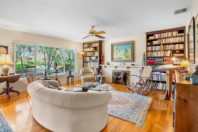 living room featuring ceiling fan, built in features, a brick fireplace, and light hardwood / wood-style flooring