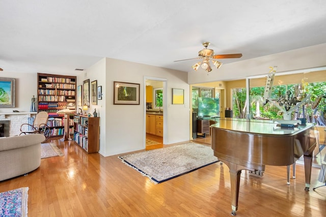 misc room with ceiling fan, a fireplace, and light wood-type flooring