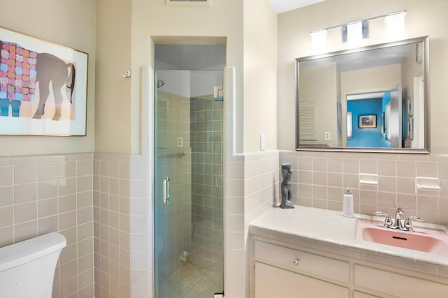 bathroom with vanity, toilet, a shower with door, and tile walls