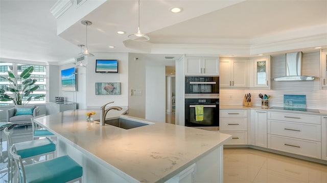 kitchen featuring tasteful backsplash, wall chimney exhaust hood, black electric stovetop, double oven, and a sink