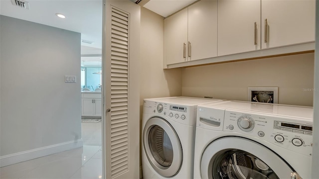 clothes washing area with light tile patterned floors, cabinet space, visible vents, washer and dryer, and baseboards