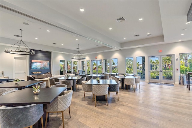 dining space featuring a raised ceiling, light wood-type flooring, and french doors