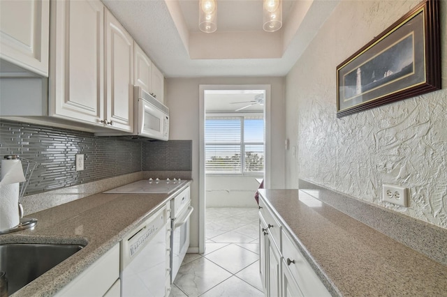 kitchen with sink, white appliances, white cabinetry, backsplash, and a raised ceiling