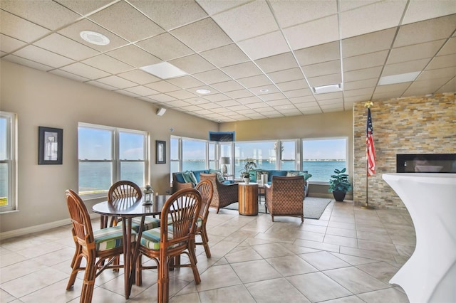 dining space with light tile patterned flooring, a water view, and a paneled ceiling