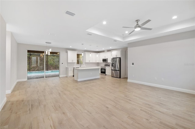 unfurnished living room with ceiling fan, a tray ceiling, sink, and light hardwood / wood-style flooring