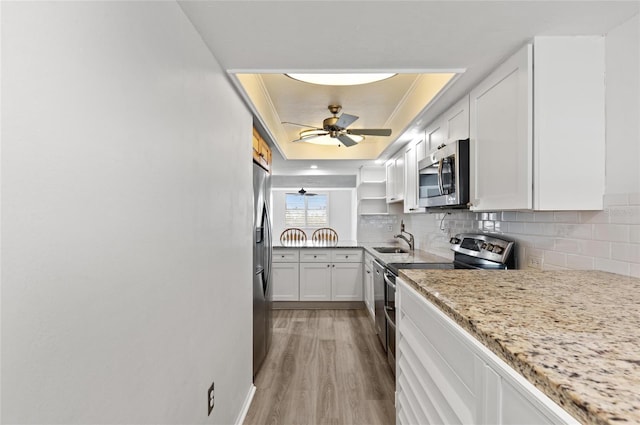 kitchen featuring sink, stainless steel appliances, light stone counters, a tray ceiling, and white cabinets