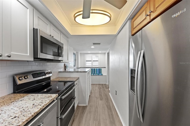 kitchen with appliances with stainless steel finishes, white cabinetry, decorative backsplash, light stone counters, and light wood-type flooring