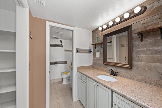 bathroom with wood walls, tile patterned flooring, vanity, toilet, and a textured ceiling